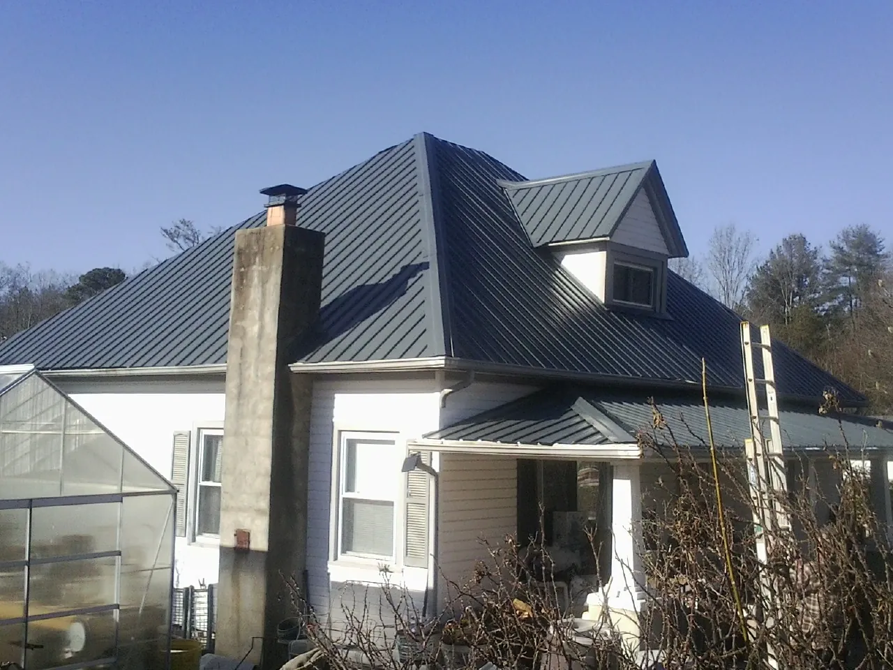 Dark blue standing seam metal roof on a white farmhouse with dormer in Pleasant Grove