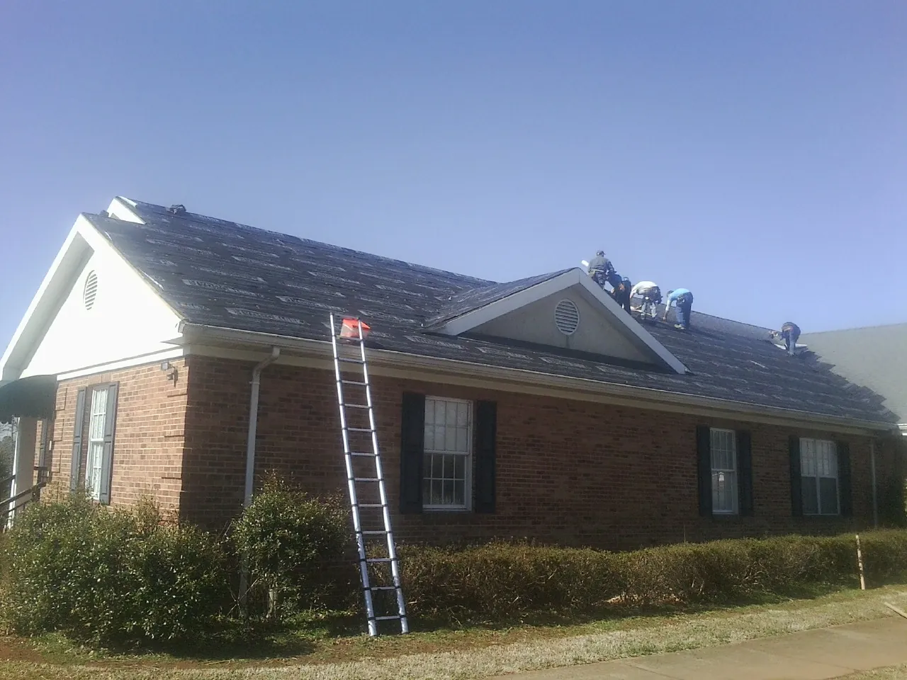 Crew tearing shingles off a brick ranch roof with a ladder set — Emergency Roof Repair work by our crew in Pleasant Grove