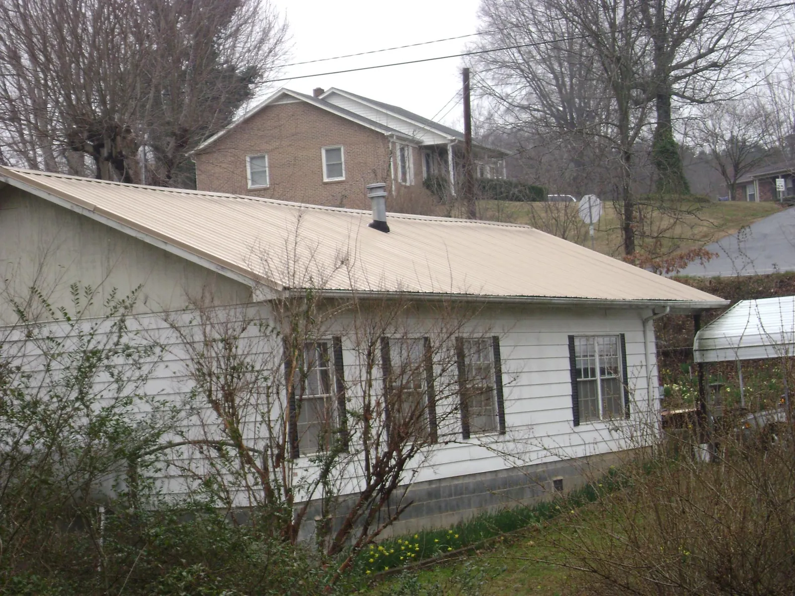 Tan metal roof on a white sided house set into a hillside — Commercial Roofing by Roofing Brothers in Pleasant Grove